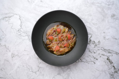 Spicy tom yum soup in a black plate on a marble table background. Traditional Japanese food menu