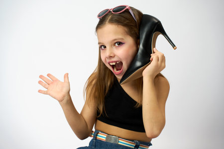 Cute girl using a shoe like a telephone holding it in her face and talking, white background. Shopping sale, promotion, fashion and people concept.の写真素材