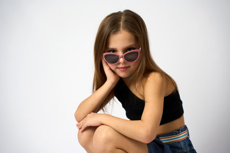 Portrait of a cute girl wearing sunglasses and denim skirt with summer top. Child girl posing on a white background with copy spaceの写真素材