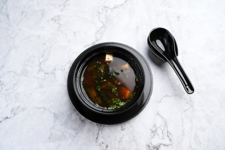 Japanese soup miso in a black bowl, top view. Miso soup on a marble background with copy space