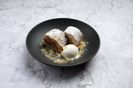 Sweet apple strudel with vanilla ice cream on a black plate on marble background with copy space.の写真素材
