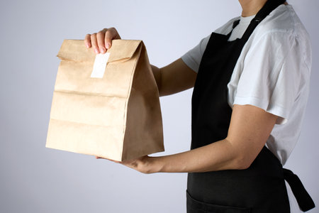 Takeaway food and delivery service. Woman holding take away paper bag over white background, close-upの写真素材