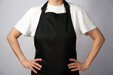 Woman in apron keeping hands on hips, close-up. White background, copy space on apron for menu