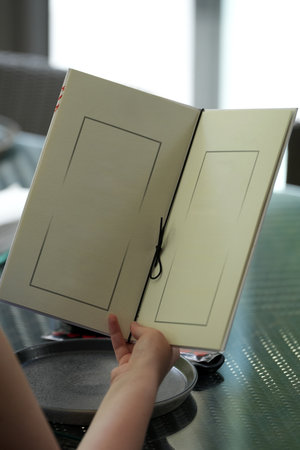 Woman holding blank menu sitting at table in a restaurant, rear view, close-up