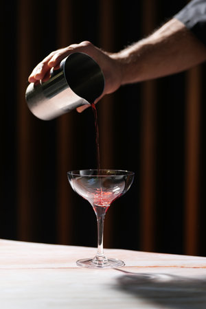 Barman pours cocktail from shaker into glass. Bartender hand pouring fresh alcoholic drink into the...