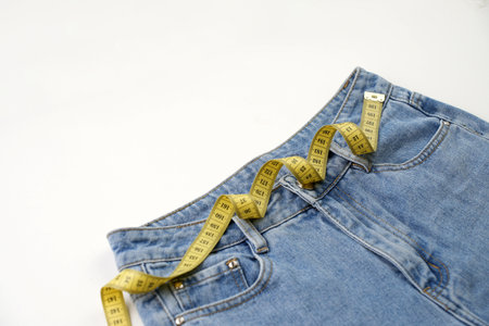 Jeans and measuring tape on a blue background with copy space, close-up. Weight loss and diet conceptの写真素材