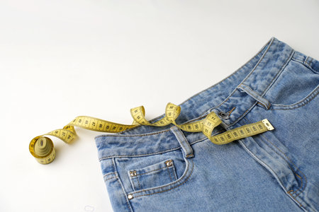 Jeans and measuring tape on a blue background with copy space, close-up. Weight loss and diet conceptの写真素材