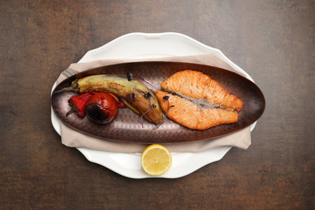 Baked salmon grilled eggplant tomato and lemon on a plate leaves on a brown backgroundの写真素材