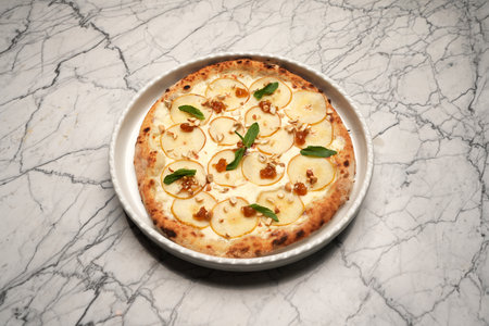 Pizza with pears, herbs and cheese on a white plateの写真素材