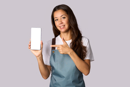 Happy woman wearing apron showing the smartphone white screen, shopping conceptの写真素材