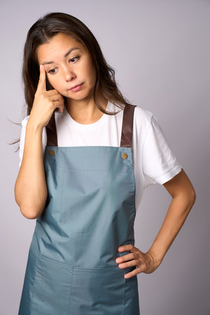 Young woman in apron thinking about something looking downの写真素材