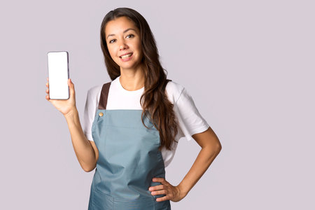 Happy woman wearing apron showing the smartphone white screen, shopping conceptの写真素材
