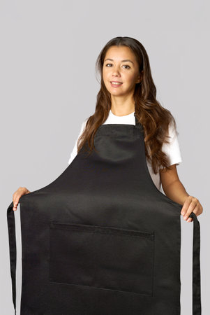 Young woman wearing apron standing. Female chef wearing apron, grey backgroundの写真素材