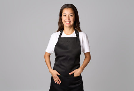 Friendly waitress, female barista in black apron. Young woman wearing black apron and white shirt standing on a white background with copy spaceの写真素材