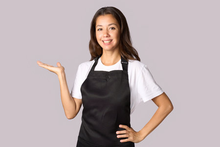 Smiling woman in apron introduce new product. Young woman wearing apron, pointing leftの写真素材