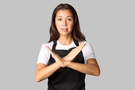 Young woman in apron showing stop gesture crossed hands isolated on gray background Process cooking food conceptの写真素材