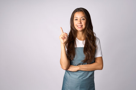 Happy woman in apron presenting isolated on white background with copy space. Beautiful smiling woman wearing apron, pointing to empty space with fingerの写真素材