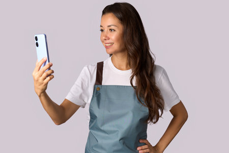 Young woman wearing apron, using smartphoneの写真素材