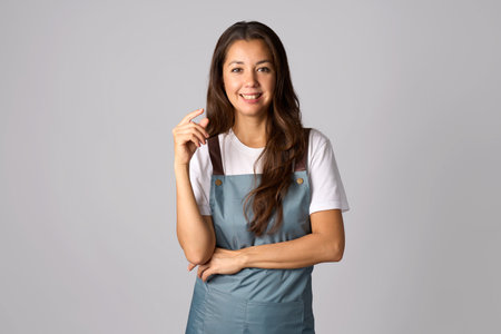 Portrait of a beautiful brunette woman wearing apron, standing on a grey background with copy spaceの写真素材