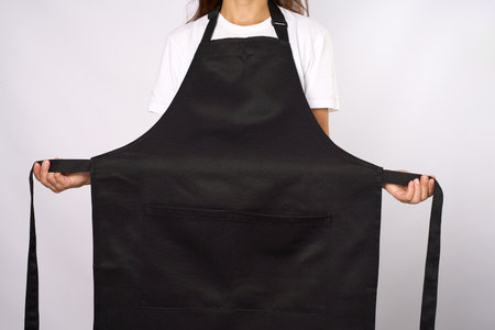 Portrait of a woman in black apron. Young female wearing apron, standing on gray backgroundの写真素材