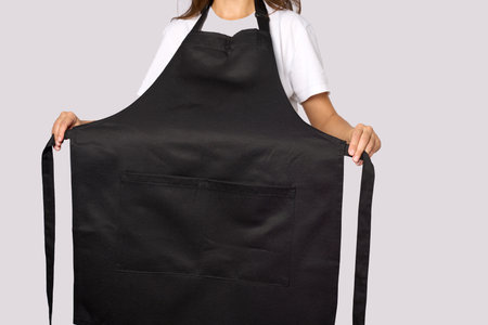 Portrait of a woman in black apron. Young female chef wearing apron, standing on gray backgroundの写真素材