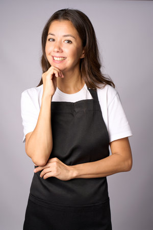 Vertical portrait of a happy woman in black apron and white shirt on a gray backgroundの写真素材