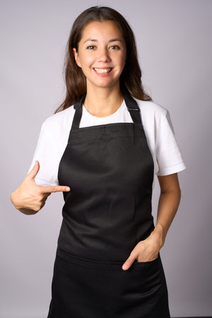 Young woman wearing black apron pointing on apron with fingerの写真素材