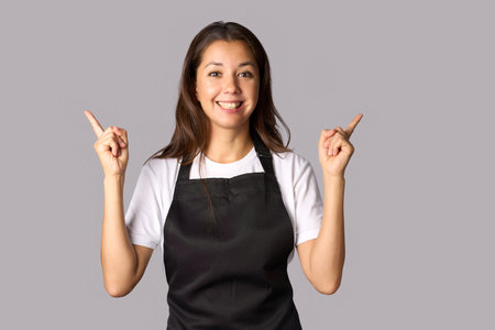 Happy woman wearing apron, standing with fingers pointing upの写真素材