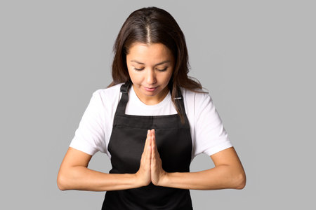 Young woman barista in apron showing namaste gesture and smiling isolated on white backgroundの写真素材
