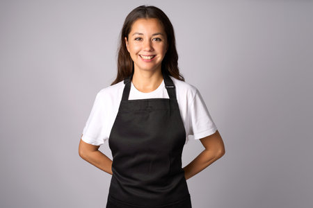 Friendly waitress, female barista in black apron. Young woman wearing black apron and white shirt standing on a white background with copy spaceの写真素材