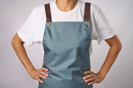Young woman in apron standing, putting her hands on her hips. Female chef wearing apron, white background, close-upの写真素材