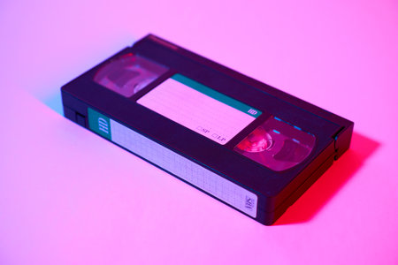Videocassette in neon light on a pink background.