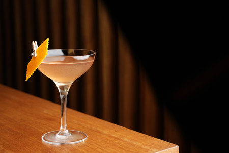 Bronx cocktail glass with orange peel slice on a wooden bar counter, background with copy spaceの写真素材