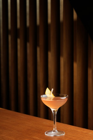 Bronx cocktail glass with orange peel slice on a wooden bar counter, background with copy spaceの写真素材