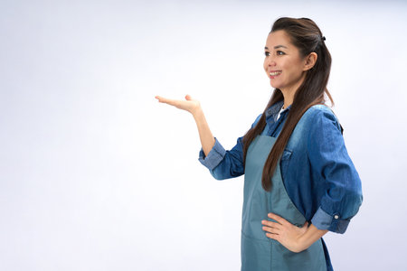 Portrait of young woman in apron standing, presenting your product on a white background with copy spaceの写真素材