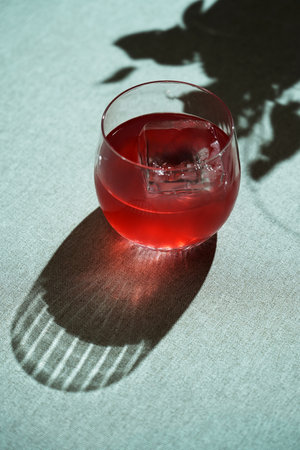 A glass of red cocktail with a large ice cube. Refreshing summer beverage on a light green background with copy spaceの写真素材