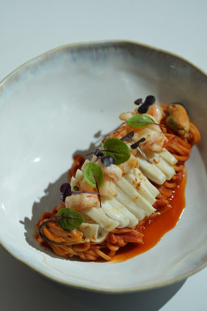 A plate of pasta with seafood. The pasta is topped with shrimp, mussels, and squid in sauce