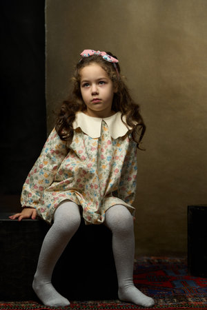 Portrait of Young Girl with Floral Headband. Cute girl with long curly hair and a floral headband sits with a calm expression against a textured backgroundの写真素材