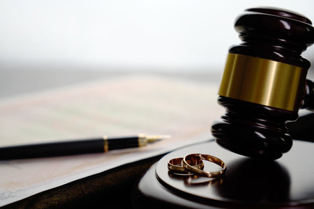 Close-up of two wedding rings, judge gavel, marriage certificate, glasses, and a fountain pen in the background. Symbol of divorce proceedings, legal separation, family law, or marriage registrationの写真素材