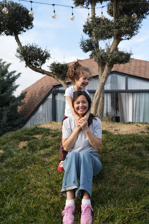 Young Daughter Playing Peek-a-Boo with Her Mother Outdoors. A young girl with curly hair covers her smiling mother's eyes with her hands, playing peek-a-boo outdoorsの写真素材