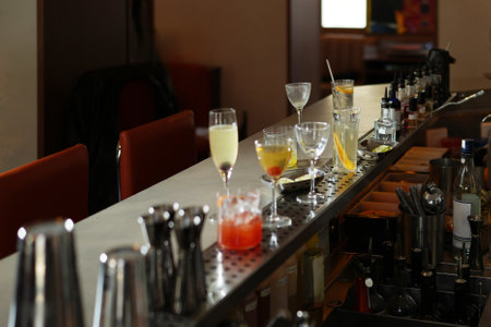 Bar counter with multiple cocktail glasses, some containing drinks, and bar tools, close-upの写真素材