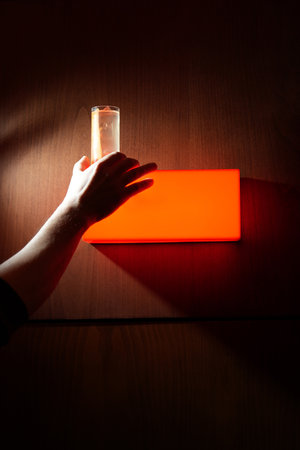 Hand holding a glass illuminated by orange lightの写真素材