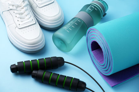 Fitness gear including a sports water bottle, jump rope, running shoes, and an exercise mat. Active lifestyle, home workout, healthy habits, and physical training. Gym preparation, cardio trainingの写真素材