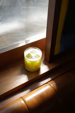 Vibrant yellow cocktail served in a rocks glass filled with ice. The drink has a frothy, white top.の写真素材
