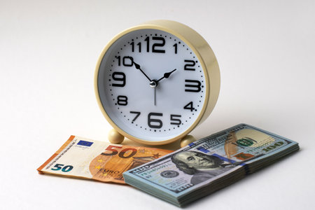 Close-up of a alarm clock with Euro and US Dollar banknote on a white background. Time and money, financial planning, global currency, investment, exchange rates, and time managementの写真素材