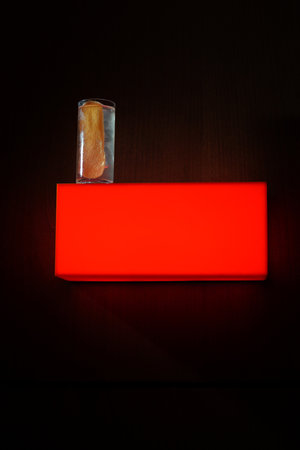 A small glass with some items inside it is placed on a red box on a dark background.の写真素材