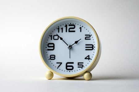 Round alarm clock with a vintage yellow or light cream casing. The clock has a white face with clear, bold black numbers and arrows, white backgroundの写真素材