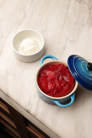 A vertical shot of a single serving dessert with red stewed fruit and vanilla ice cream in a blue...