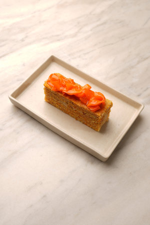A vertical shot of a rectangular slice of multilayered orange cake with cream filling, topped with...