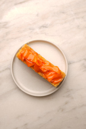 A vertical shot of a rectangular slice of multilayered orange cake with cream filling, topped with...